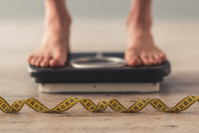 person standing on a scale with measuring tape in the foreground