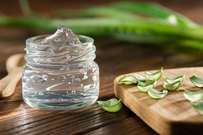 glass jar filled with aloe vera gel next to sliced aloe vera plant on cutting board