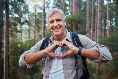 senior man making heart with hands on hike in the woods