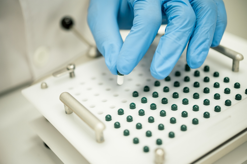 gloved hand taking compounded capsule out of pill maker